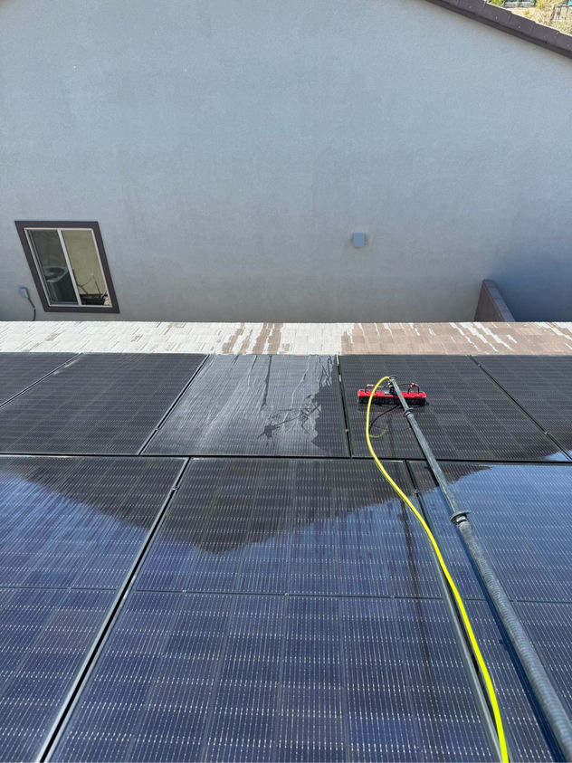 Neon Window Cleaning technician using water-fed brush to clean residential solar panels on a flat-roof Las Vegas home